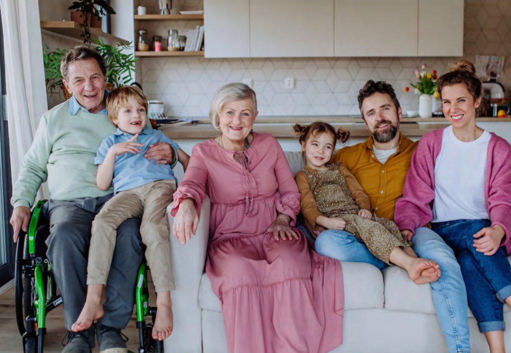 A happy family photo of parents with young children and grandparents. One of them on wheelchair.